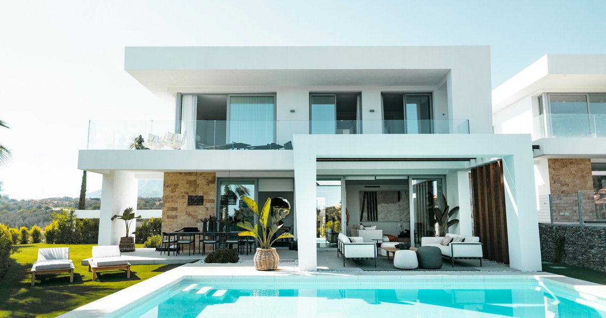 A low, single-story mid-century modern home with glass walls set into a hillside above Beverly Hills, with a view of the city below