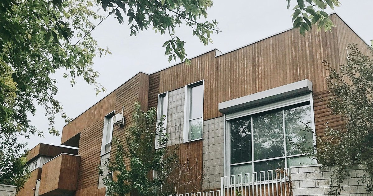 Wood-clad contemporary house with a large window and tree branches in the foreground
