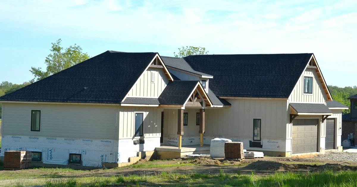 A house under construction with framing, roof, and exterior sheathing in place before finish work begins