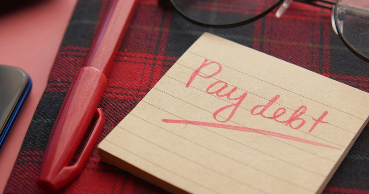 A handwritten note reading pay debt next to glasses and a pen, representing the credit recovery path after bankruptcy