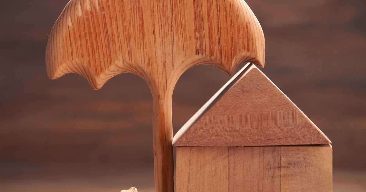A miniature wooden house sheltered by a small umbrella alongside a house key, representing homeowners insurance protection for a Dallas property