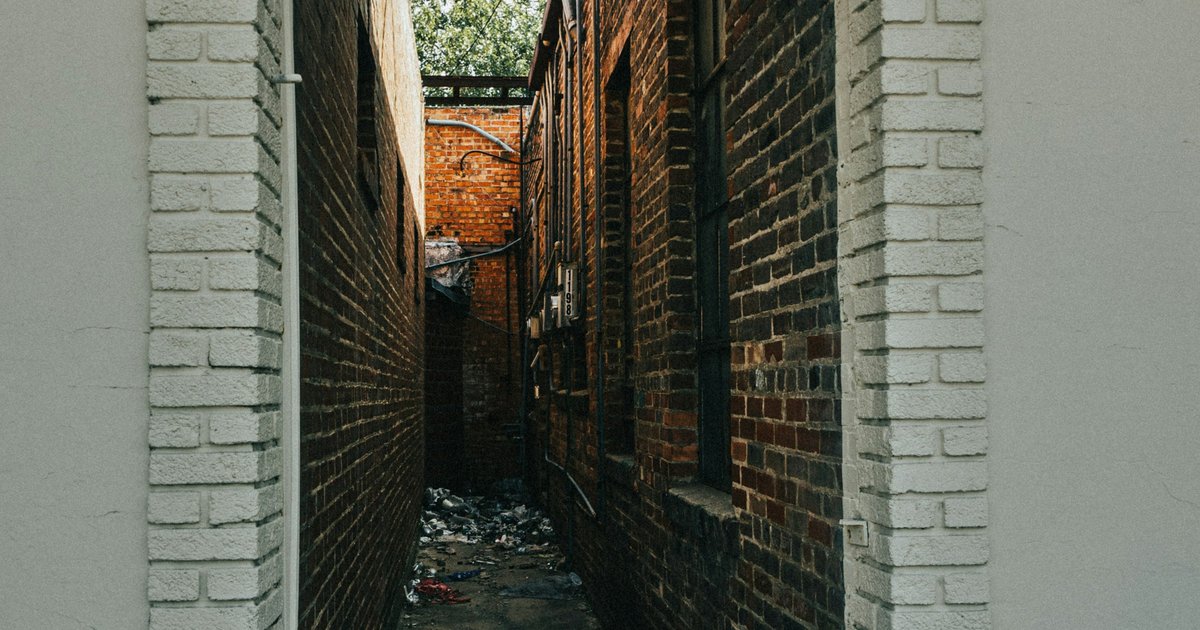 A narrow brick alley between old masonry buildings, typical of the warehouse streetscape in central Dallas