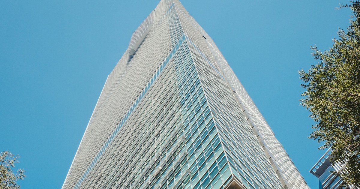 Looking up the glass facade of a high-rise tower against a clear sky, representing the high-rise condominium side of the Devonshire market