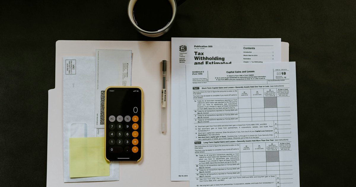 Black Android smartphone next to a ballpoint pen and a tax withholding certificate on a white folder, representing the IRS paperwork involved in a FIRPTA closing