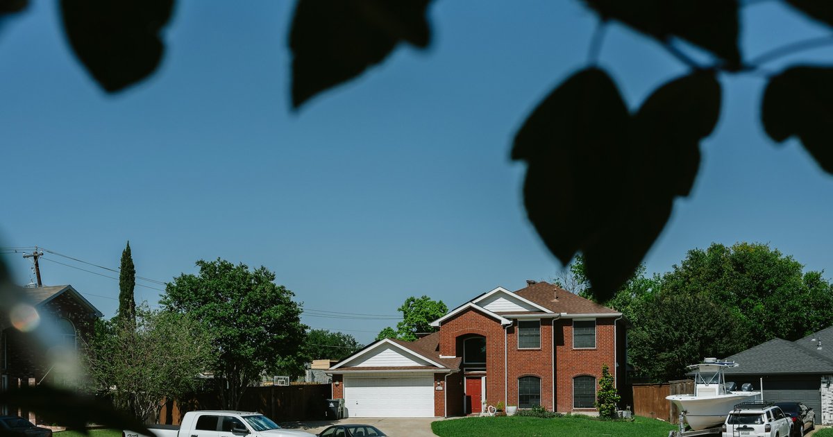 Established brick two-story home with mature trees on a residential Highland Village street