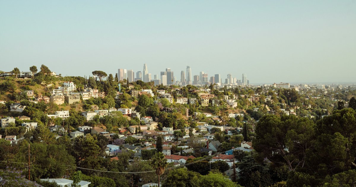Hillside homes on a wooded slope below the Hollywood Sign, with red tile roofs among the trees