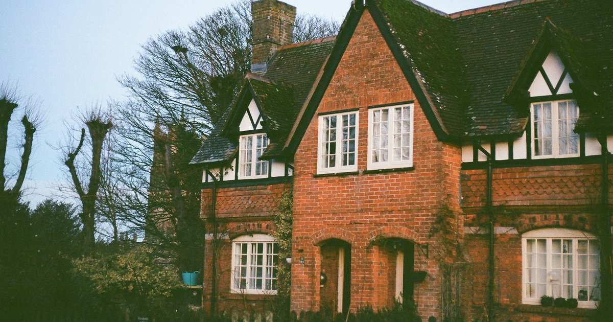 Red brick cottage with half-timbered gables and white casement windows, illustrating the Tudor cottage style common in 1920s East Dallas
