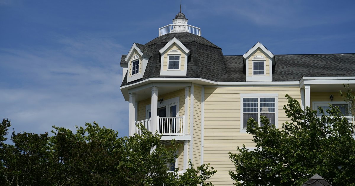 A large white 1930s-style estate house with a dark roof set behind mature trees and a manicured front lawn