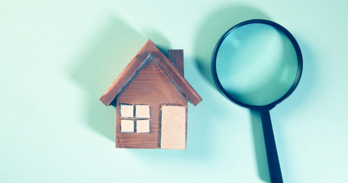 A magnifying glass positioned over a miniature wooden house model, representing the thorough TREC inspection process for DFW buyers