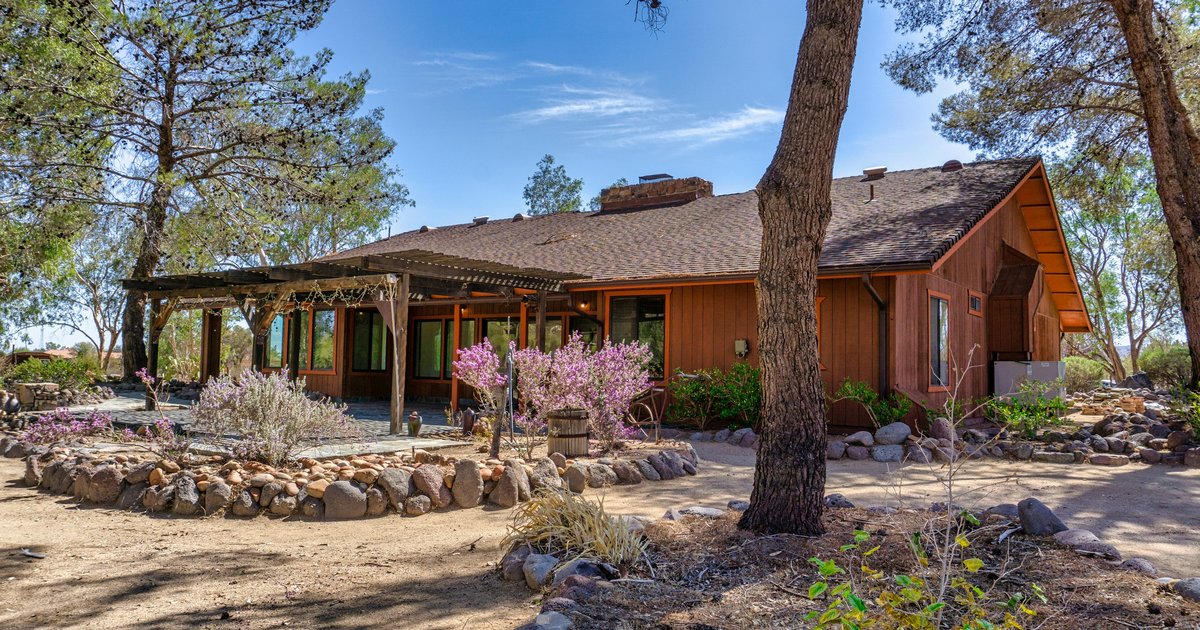 Single-story ranch-style house with a wide low roofline, wood siding, and mature trees on a level lot