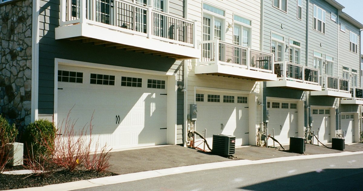 Row of attached three-story townhomes with tandem garages and second-floor balconies along a residential street