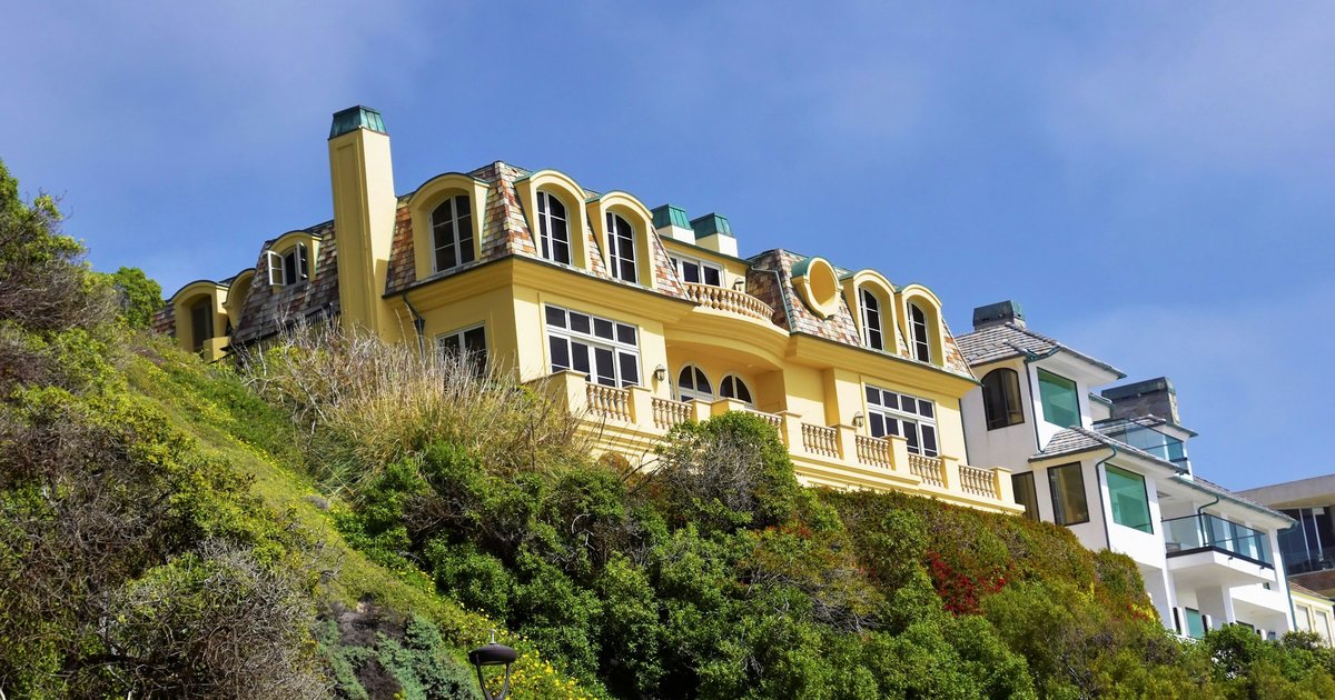 A Mediterranean-style hillside estate with white stucco walls, arched windows, and mature palm trees, similar to the architecture found in the Los Feliz Estates hillside enclave