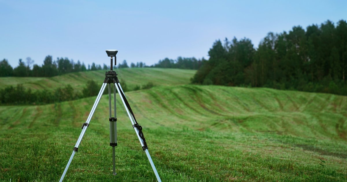A land surveyor's total station positioned in an open green field, representing professional site assessment for a DFW lot purchase