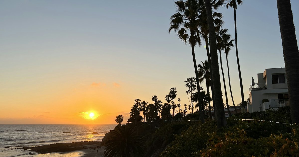 Palm trees silhouetted against a Southern California sunset over the Pacific coastline