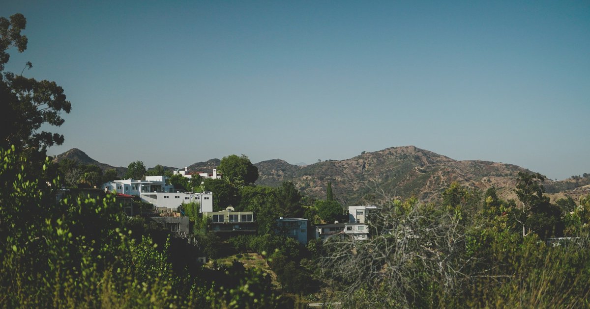 Aerial view of hillside homes tucked into a canyon slope above Los Angeles, with dense chaparral and winding roads