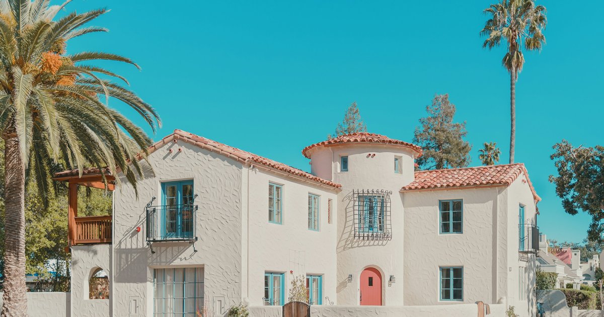 Two-story Spanish Colonial Revival house with a clay tile roof and corner turret on a palm-lined West Hollywood street
