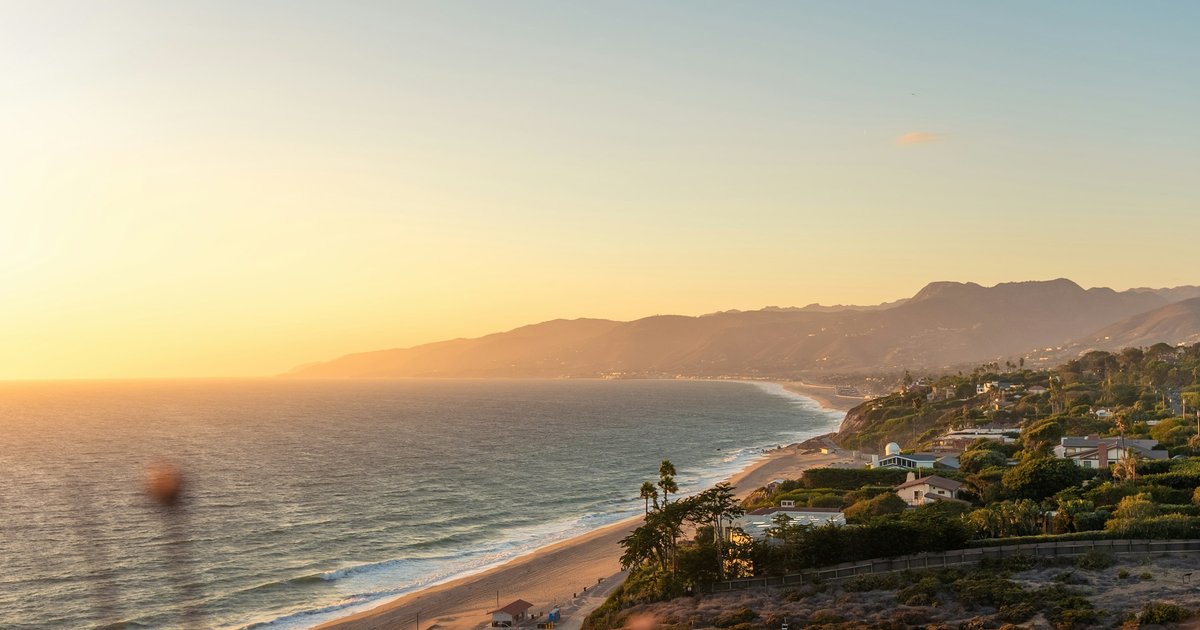 The Malibu coastline near Point Dume at sunset, with bluff-top homes above the beach and the Santa Monica Mountains behind