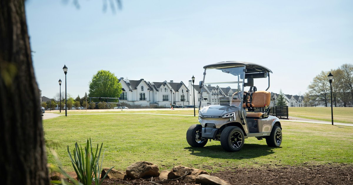 Golf cart parked on a sunny green lawn beside a fairway in a golf course community