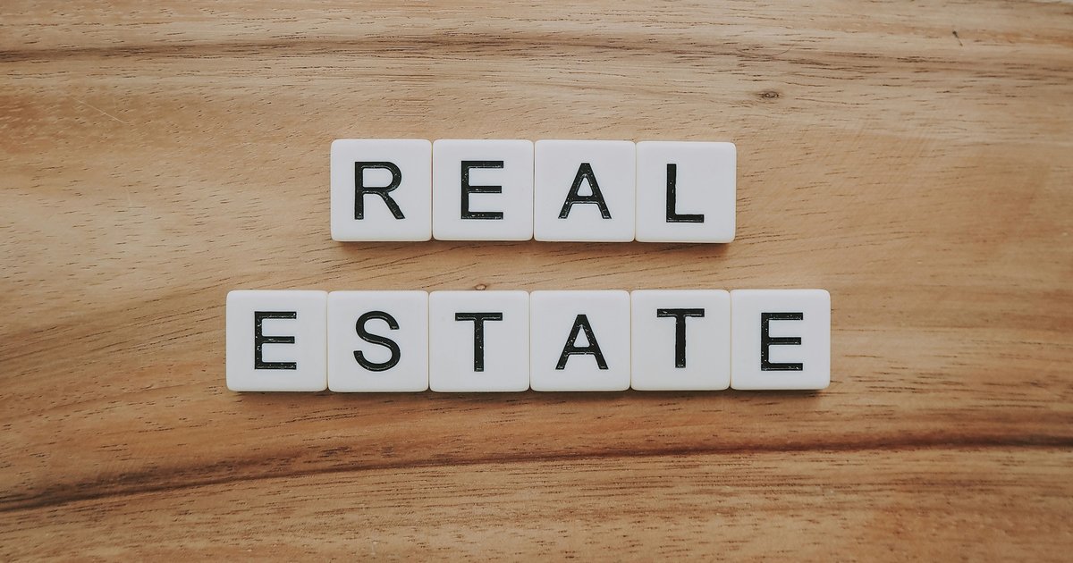 Wooden letter blocks spelling out "real estate" on a grey surface, representing property investment financing decisions