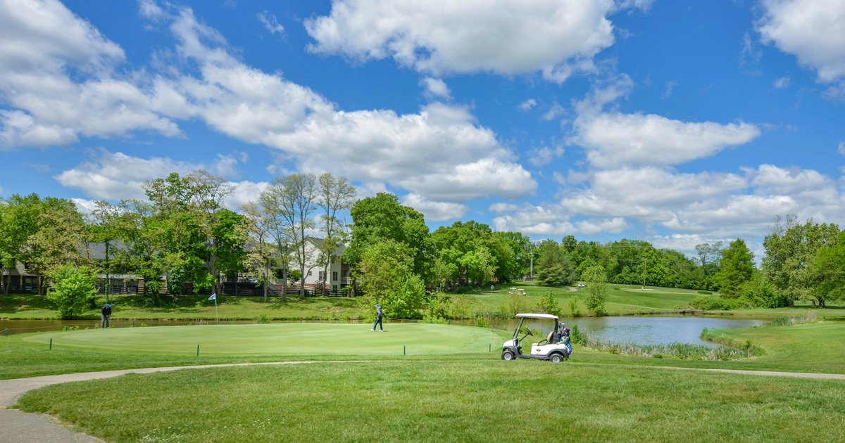 A golf course green with a pond, a cart path, and homes backing directly onto the fairway