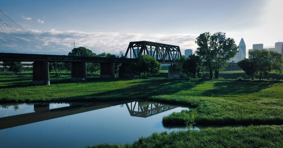 A footbridge over a small river in a Dallas park at sunrise, illustrating the green space found around the city