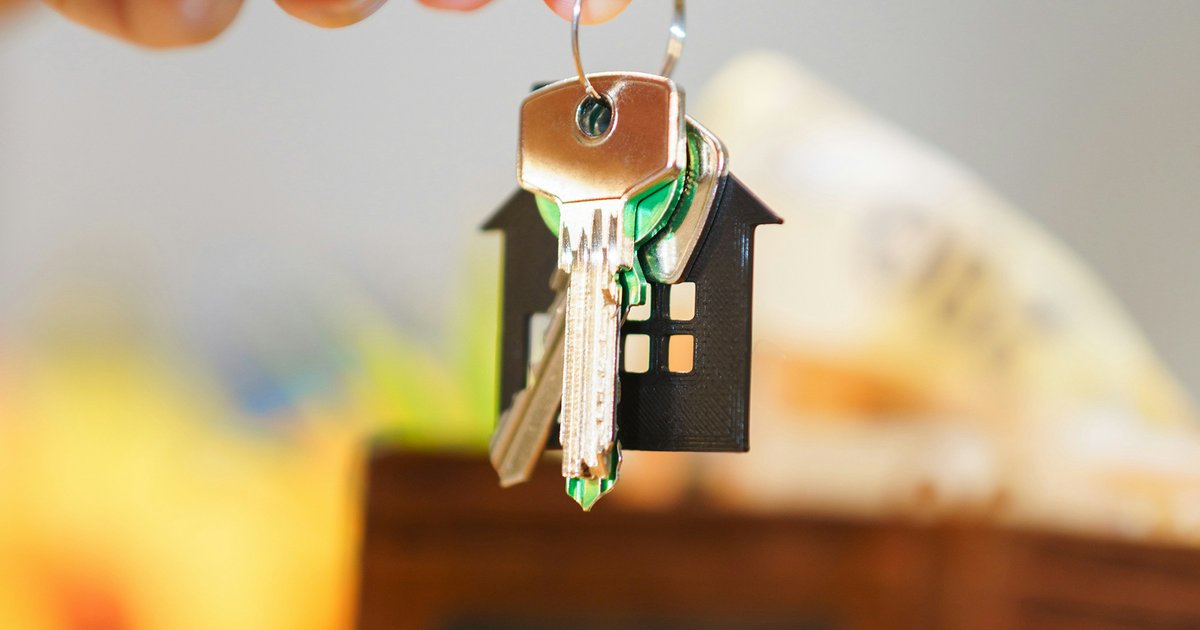 A hand holding keys with a house-shaped keychain over coins and a wallet