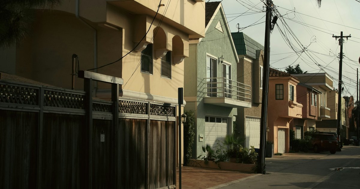A red-brick single-story house with white columns and a wrought-iron fence on a Los Angeles street