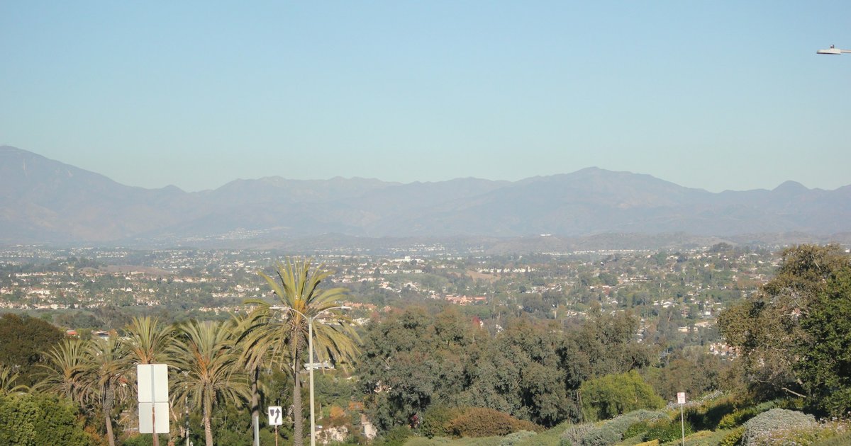 A wide Southern California boulevard cresting a rise, lined with palms and low-rise homes, with the Santa Monica Mountains in the distance