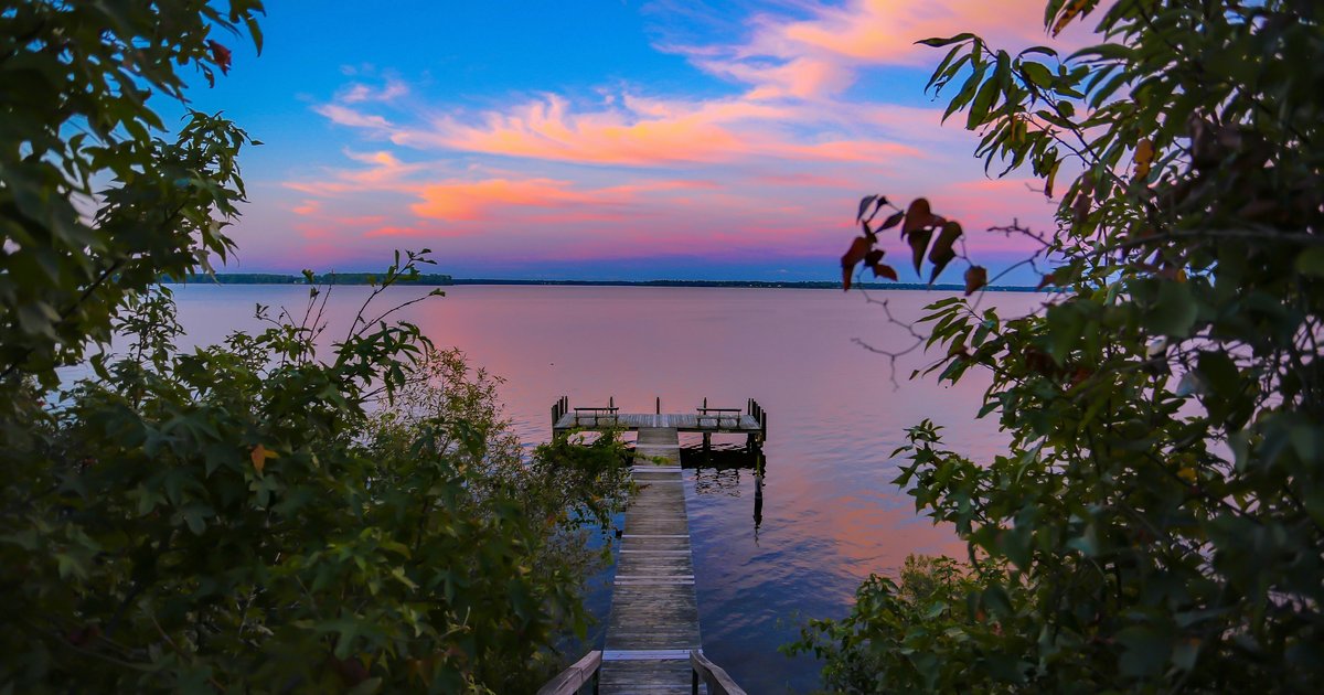 A lakeside dock at dusk under a pink and blue sky, shown for the setting of a city between two North Texas lakes