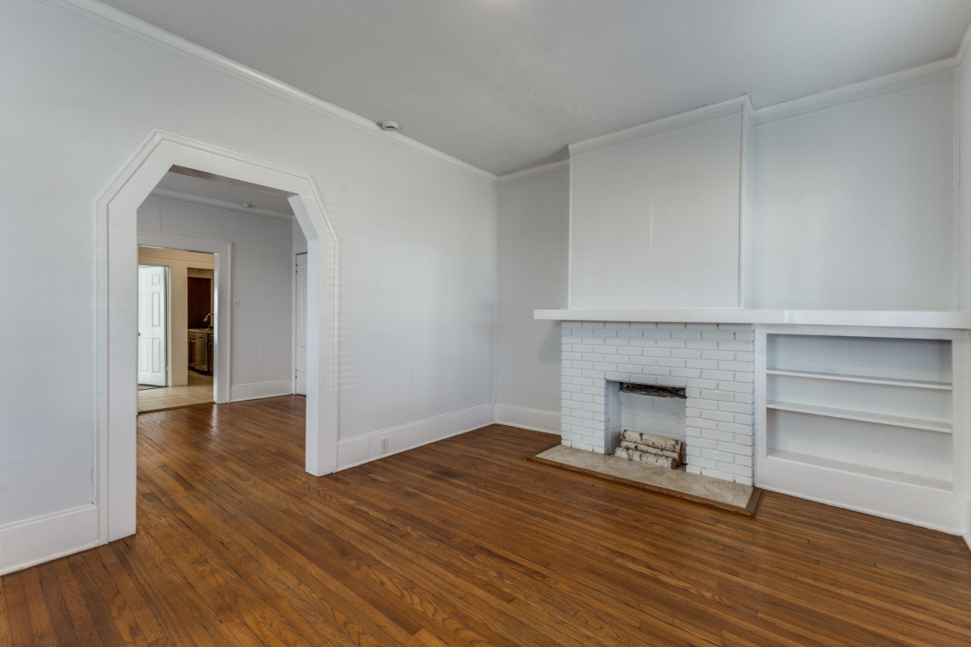 Original hardwood floors and a brick fireplace with built-in shelving inside 6010 Richmond Avenue